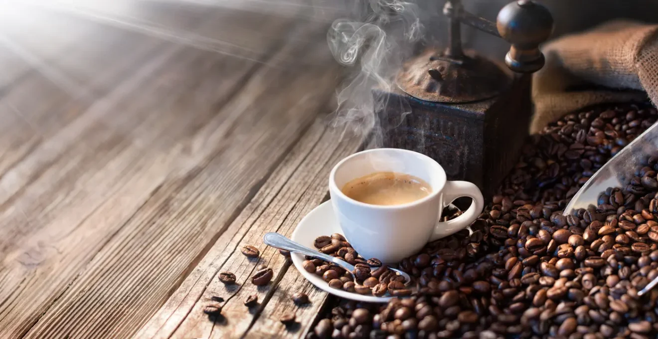 Une personne moud des grains de café avec un moulin manuel au-dessus d'un filtre V60 posé sur une carafe en verre.